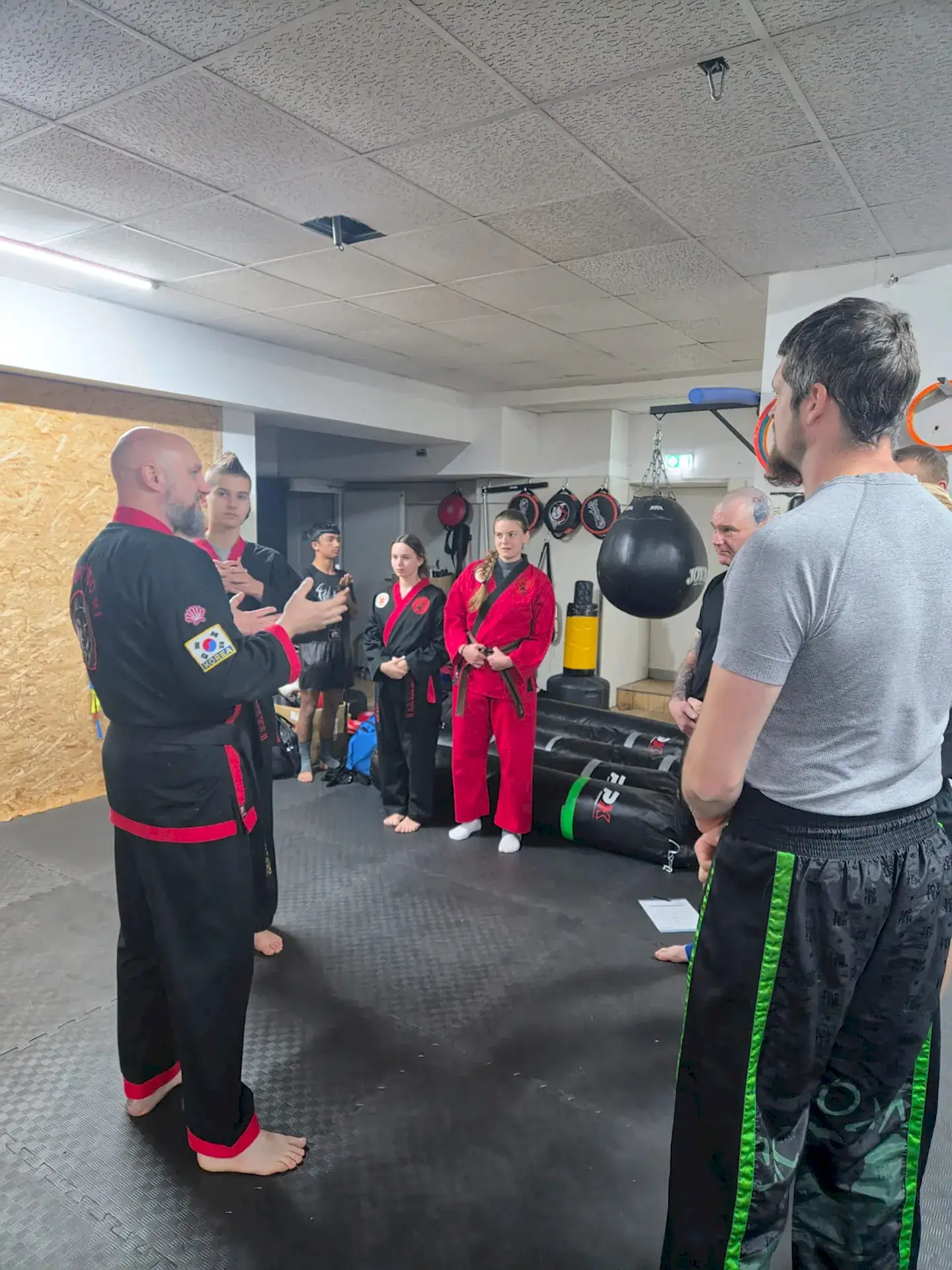 Ein Trainer erklärt mit geöffneten Händen eine Übung vor einer Gruppe in unterschiedlicher Trainingskleidung.